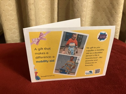Photo of a printed gift card on a yellow background, with text on the left that says: 'A gift that makes a difference: a mobility aid' To the right are two photos of disabled women in Rwanda: one a young woman using shiny aluminium crutches; one an older woman pushing a wheeled walking frame. On the right is some text saying: 'My gift to you supplies a mobility aid so a disabled person's life is transformed - like Jannette and Didancien in Rwanda'. There are logos for Through the Roof www.throughtheroof.org and their project Wheels for the World. There is also a QR code linking to their International Missions page at https://runyourownwebsite.uk/ttr/international-mission/