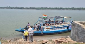 Boat moored by quay, with people walking down to get on to it. An Indian flag is flying on the boat.