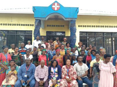 Group portrait of about 40 people in Rwanda, both men, women and children, outside a church building.