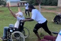The team wheelchair races, as one team member celebrates crossing the line while another pushes them