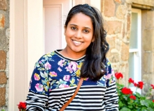 Evangeline-Thanaseelan_Smiling young woman with long dark hair, stood by a rose bush
