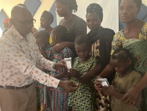 A man presenting an audio Bible to two young Rwandan children who may be blind. Their mothers stand behind them,
