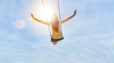 A woman on a swing, arms outstretched wide, nothing but the sky in front of her