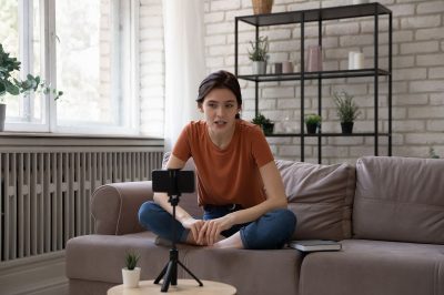 A girl sitting down, filming herself with a smartphone mounted on a tripod