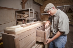 A carpenter using a chisel on a cabinet drawer in a workshop.